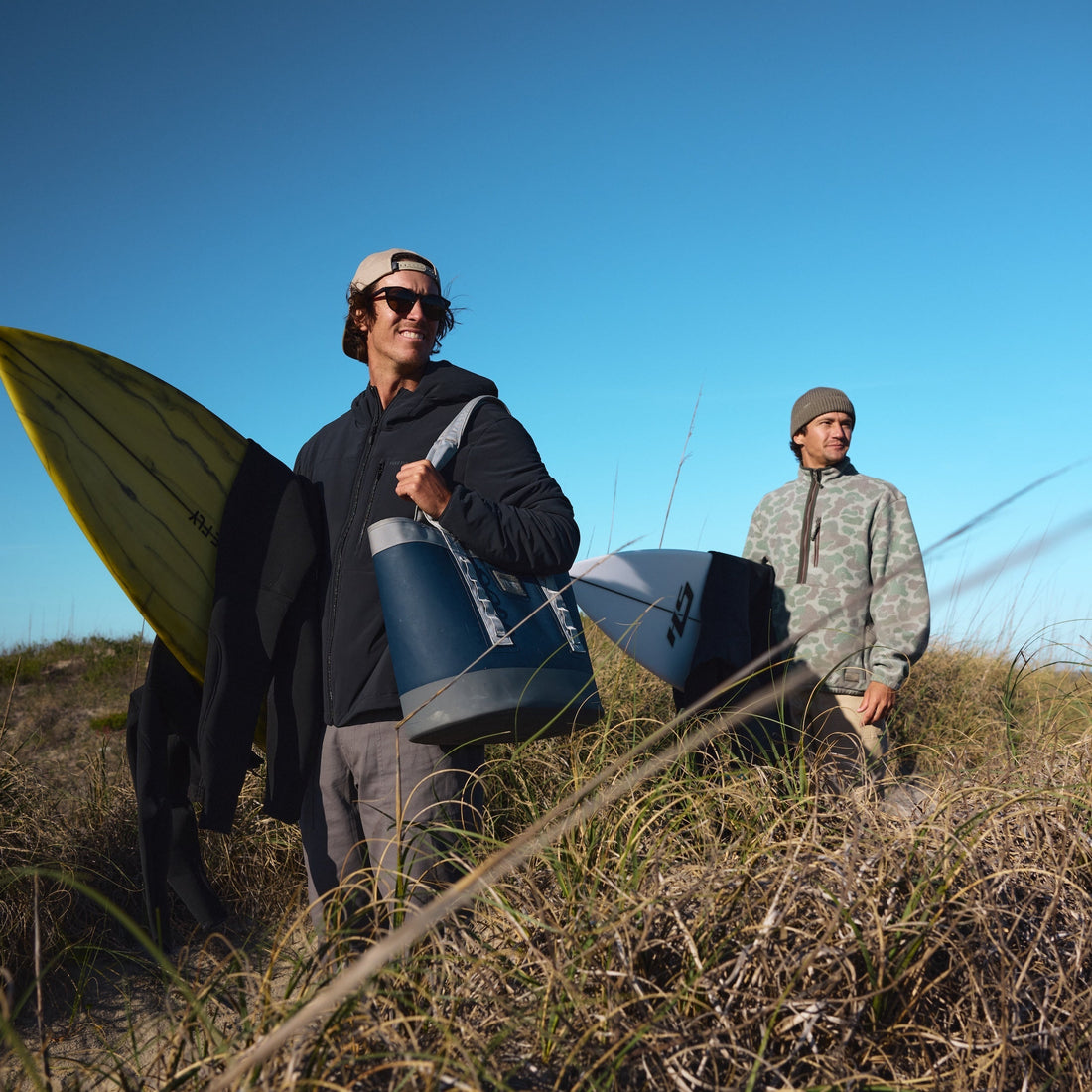 Two men in fall layers walking through dune grass, from the Fall 2026 men's guide at High Country Outfitters