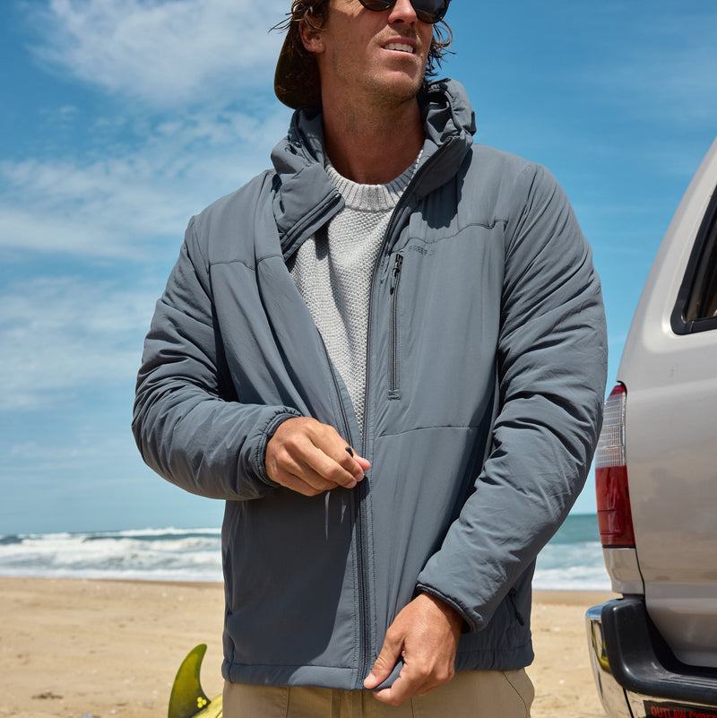 Man leaning against pole with blue vest on and long sleeve blue shirt