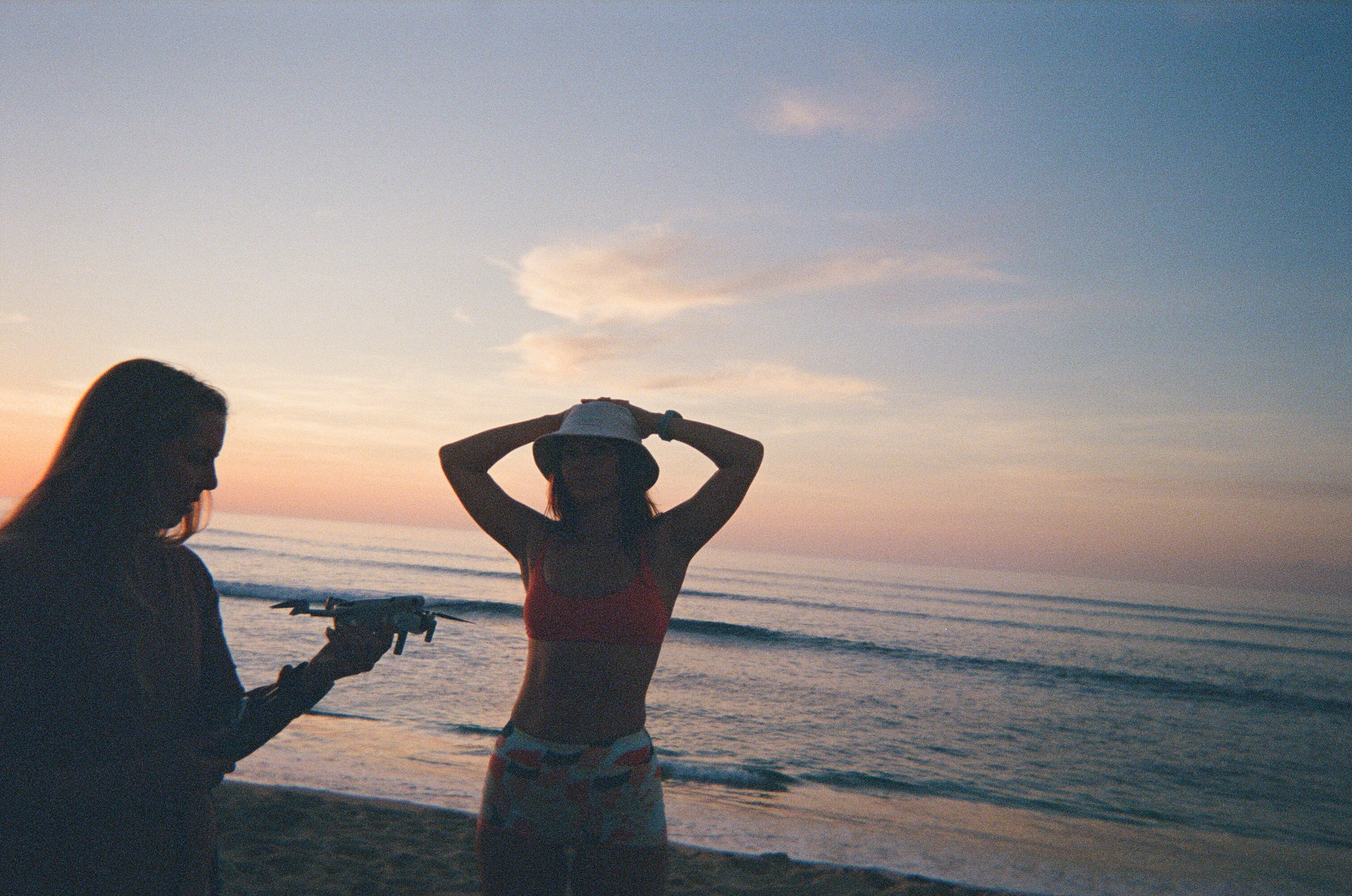 Two people on a beach at sunset, one holding a camera.