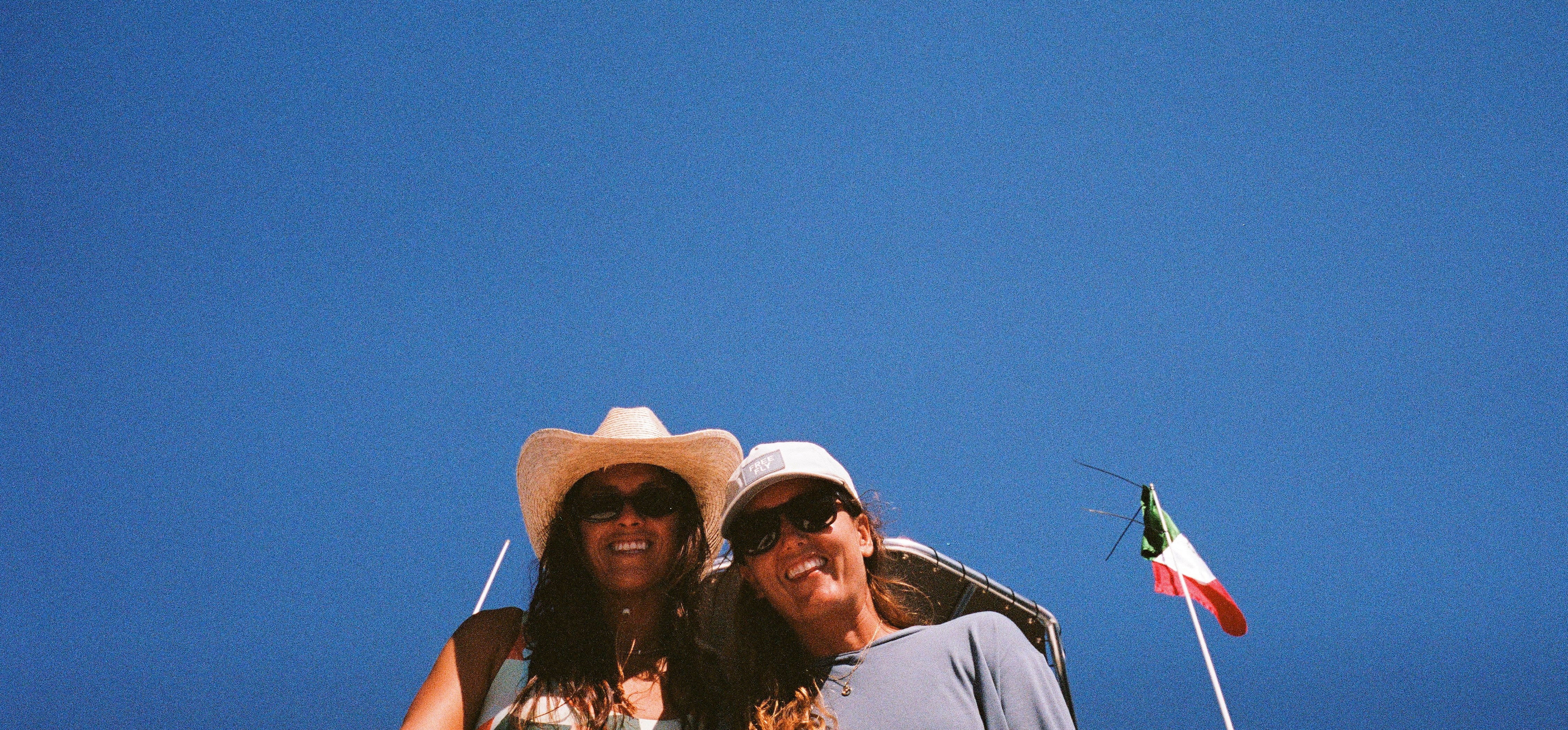 Two people wearing hats with a clear blue sky and a flag in the background