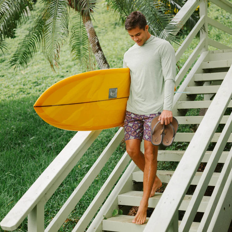 Man holding a yellow surfboard walking up a set of stairs with palm trees in the background