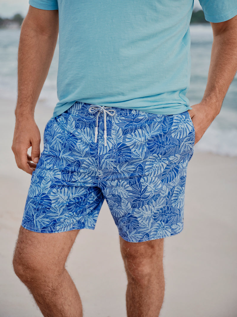Person wearing blue tropical leaf-patterned shorts and a light blue shirt on a beach.
