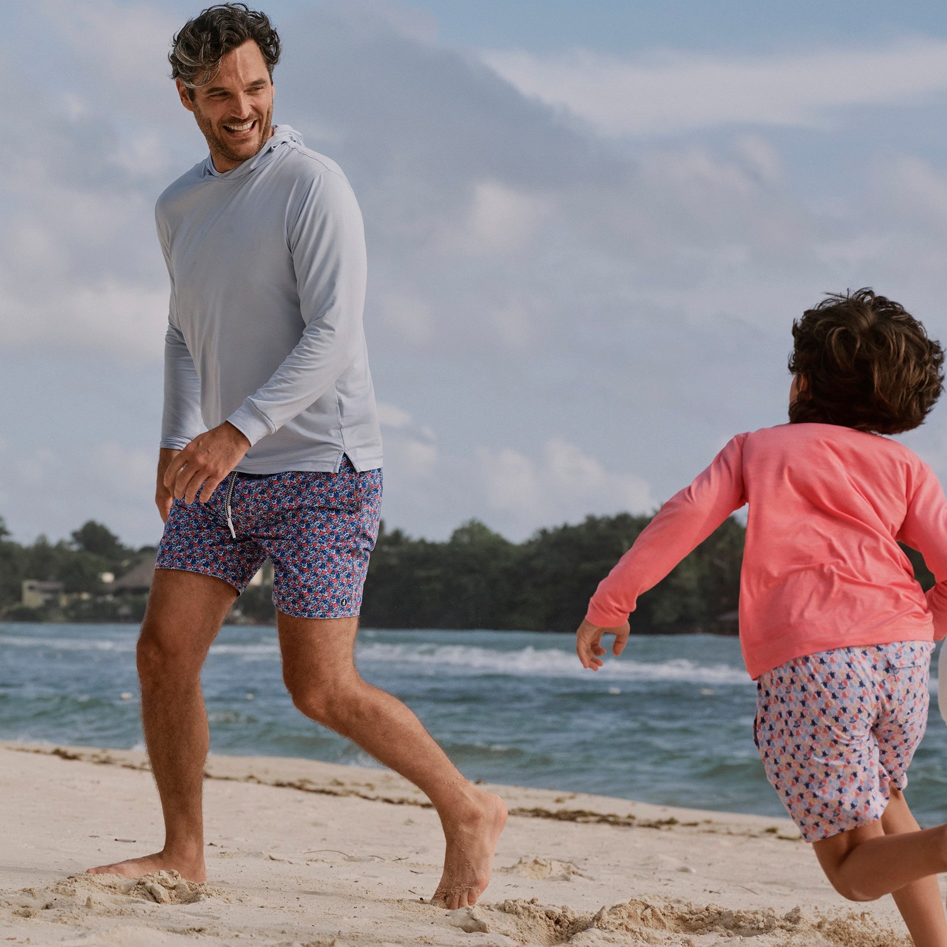 Man and child playing on a sandy beach with ocean and mountains in the background