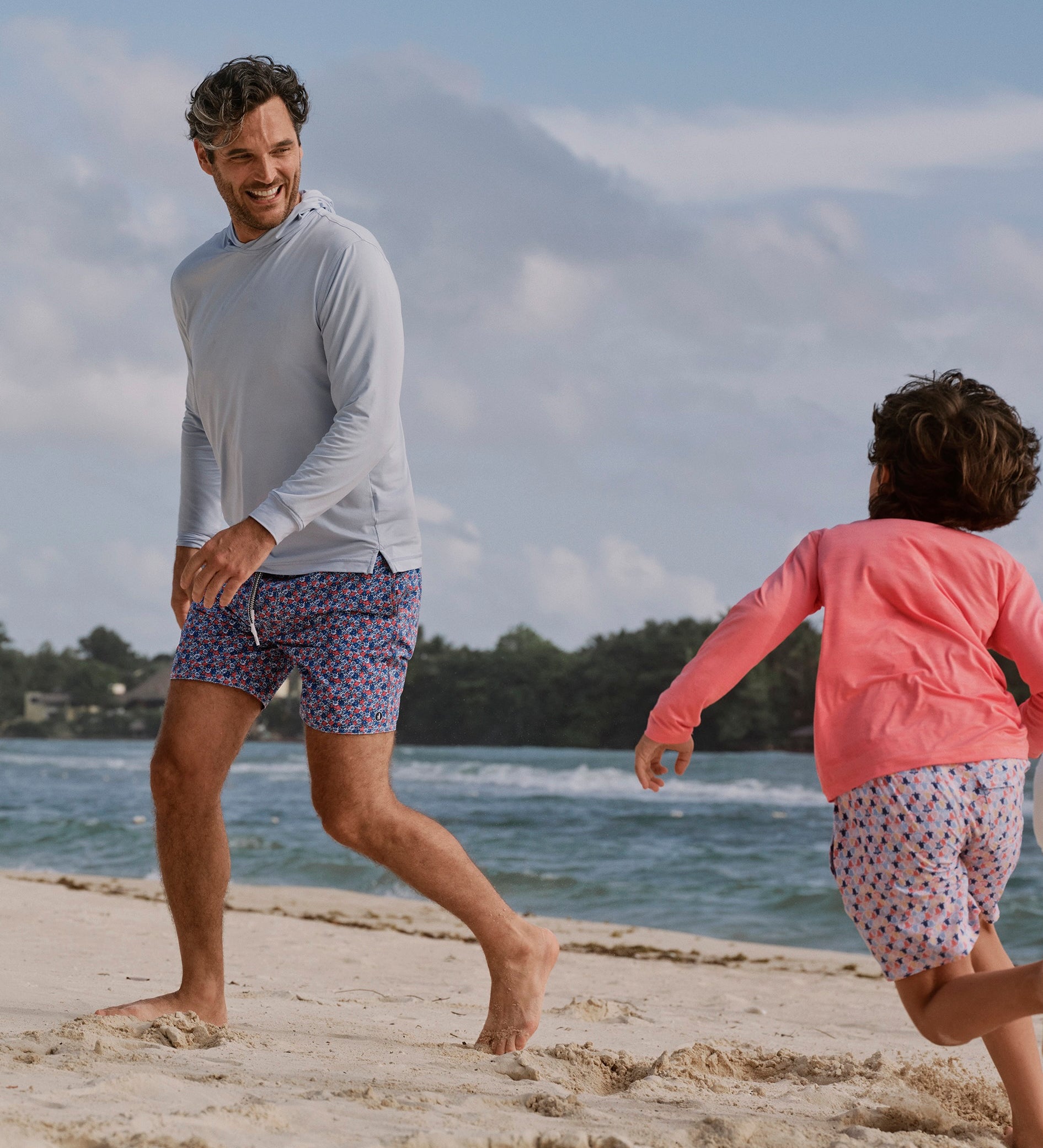 Man and child playing on a sandy beach with ocean and mountains in the background