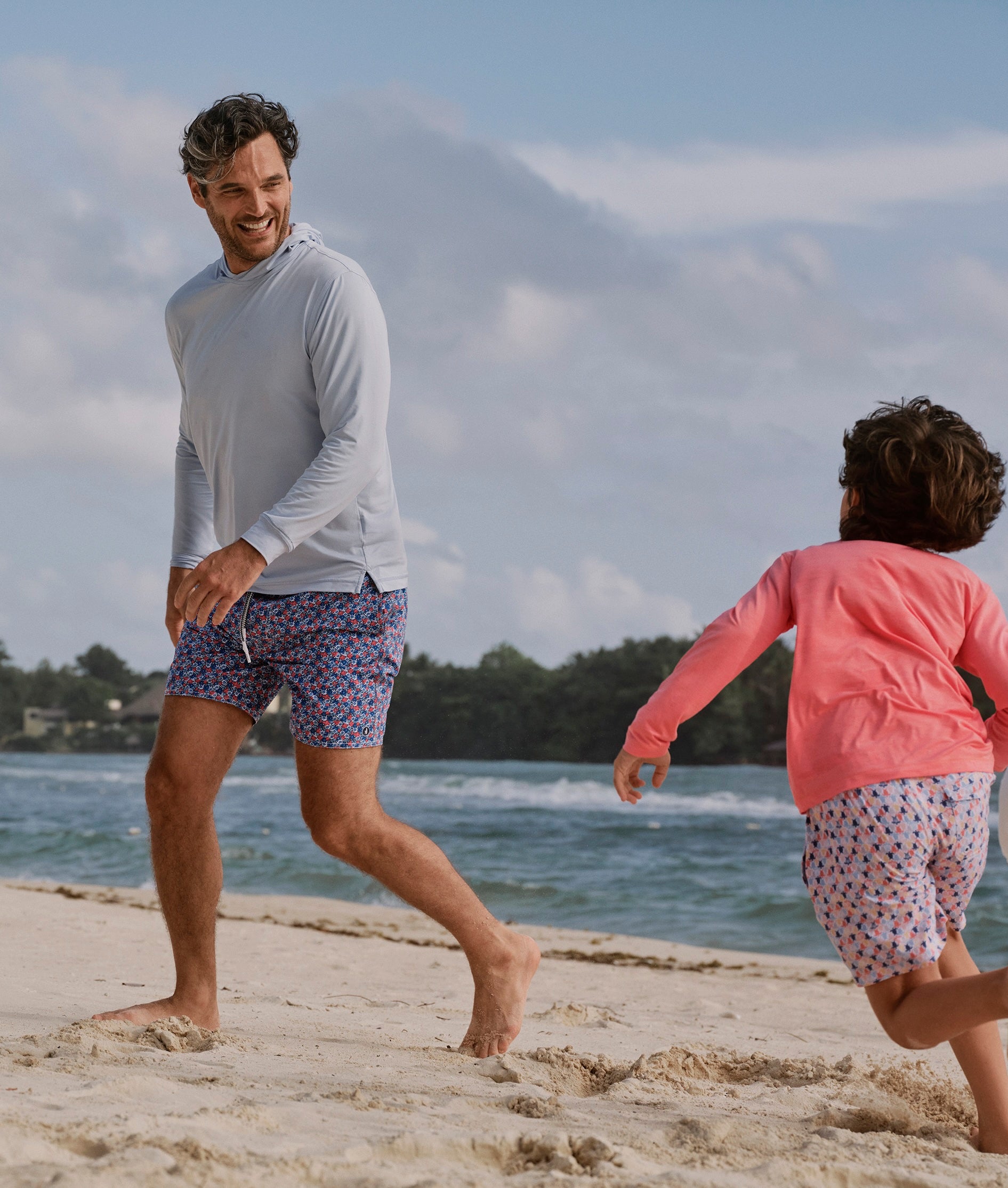 Man and child playing on a sandy beach with ocean and mountains in the background
