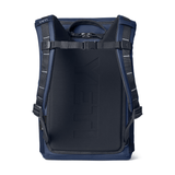 A YETI backpack shown from the back, featuring a dark navy blue padded main compartment with embossed branding, dark blue side panels, and black shoulder straps with silver reflective stitching, set against a plain white background.