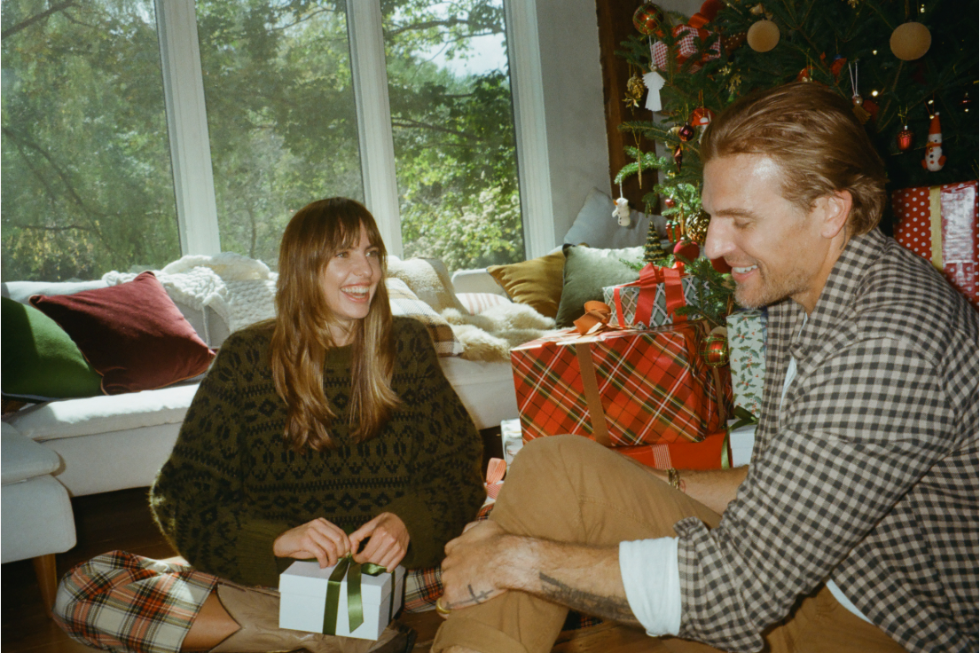 Two people sitting together in a cozy living room with a Christmas tree and presents.
