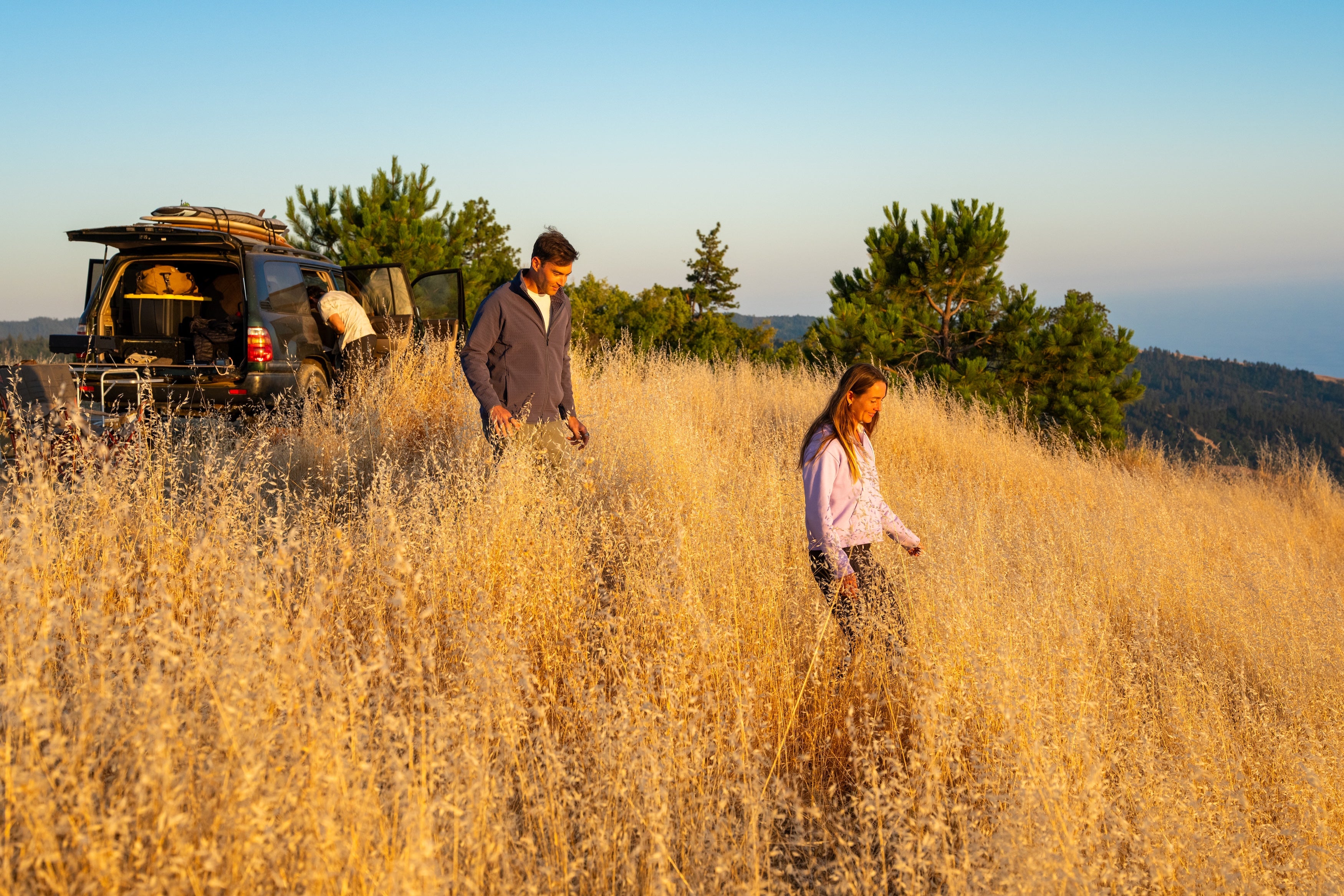 Two people walking through tall grass with a vehicle in the background