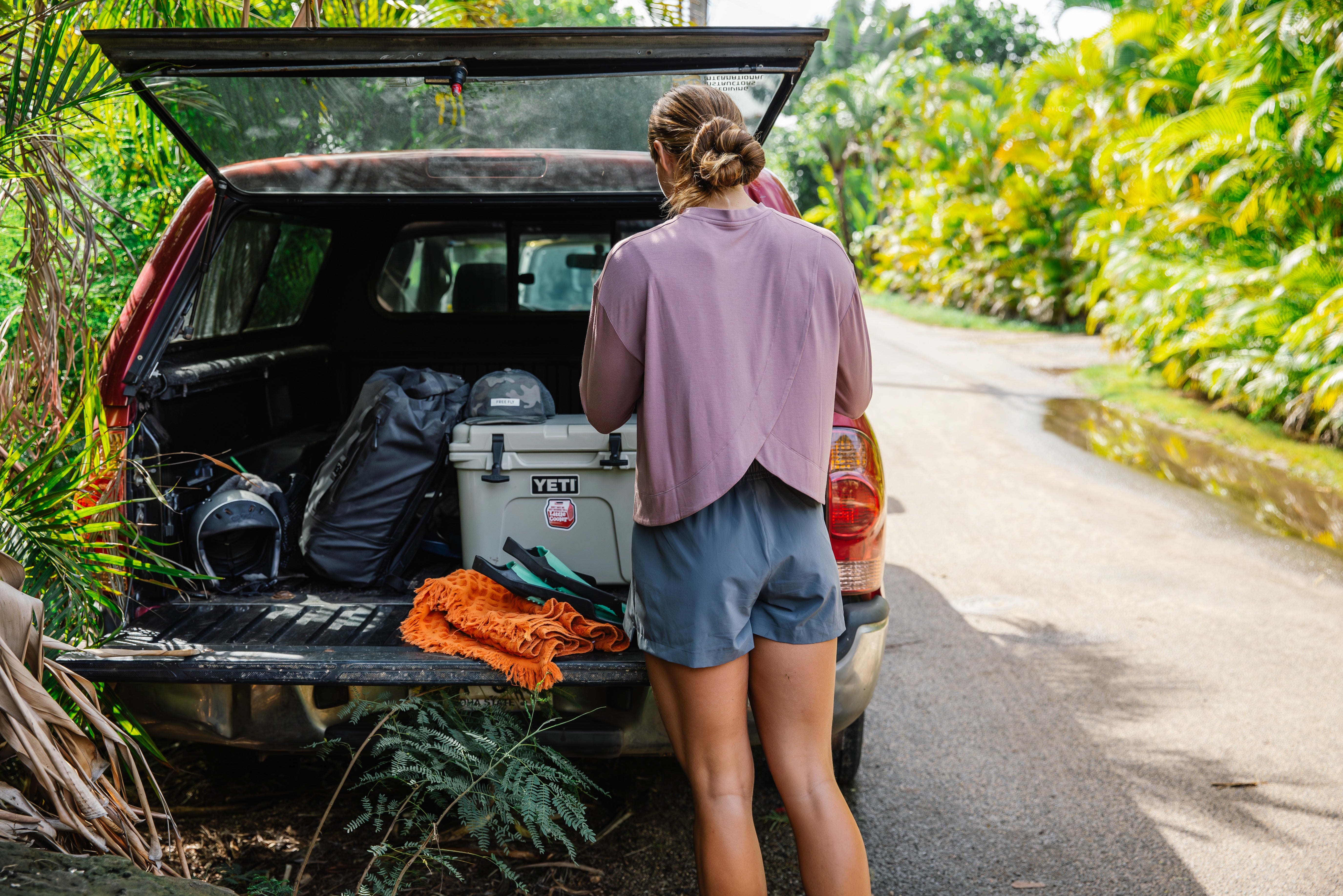 Person standing next to an open car trunk with camping gear in a natural setting