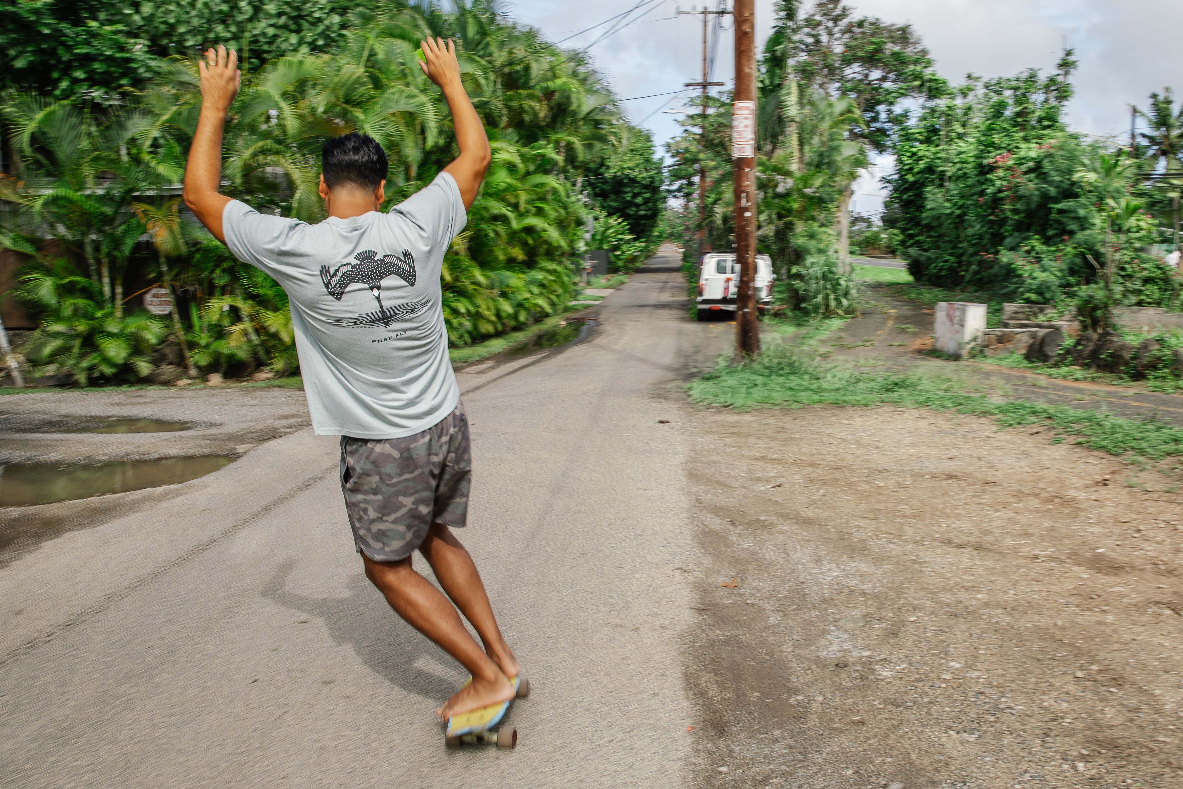 Person skateboarding down a rural road with trees and a truck in the background