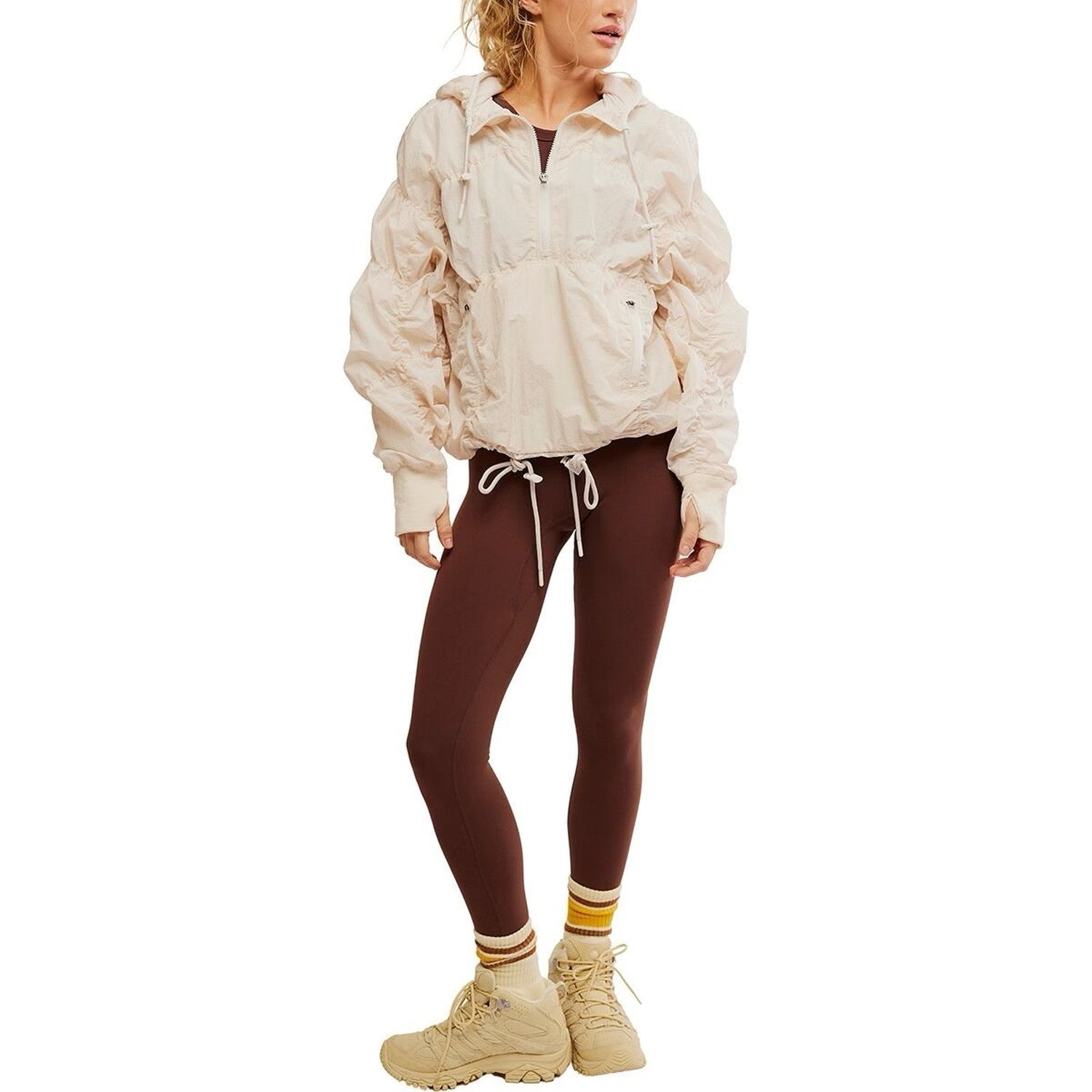 Person wearing a beige jacket, brown leggings, and beige boots on a white background