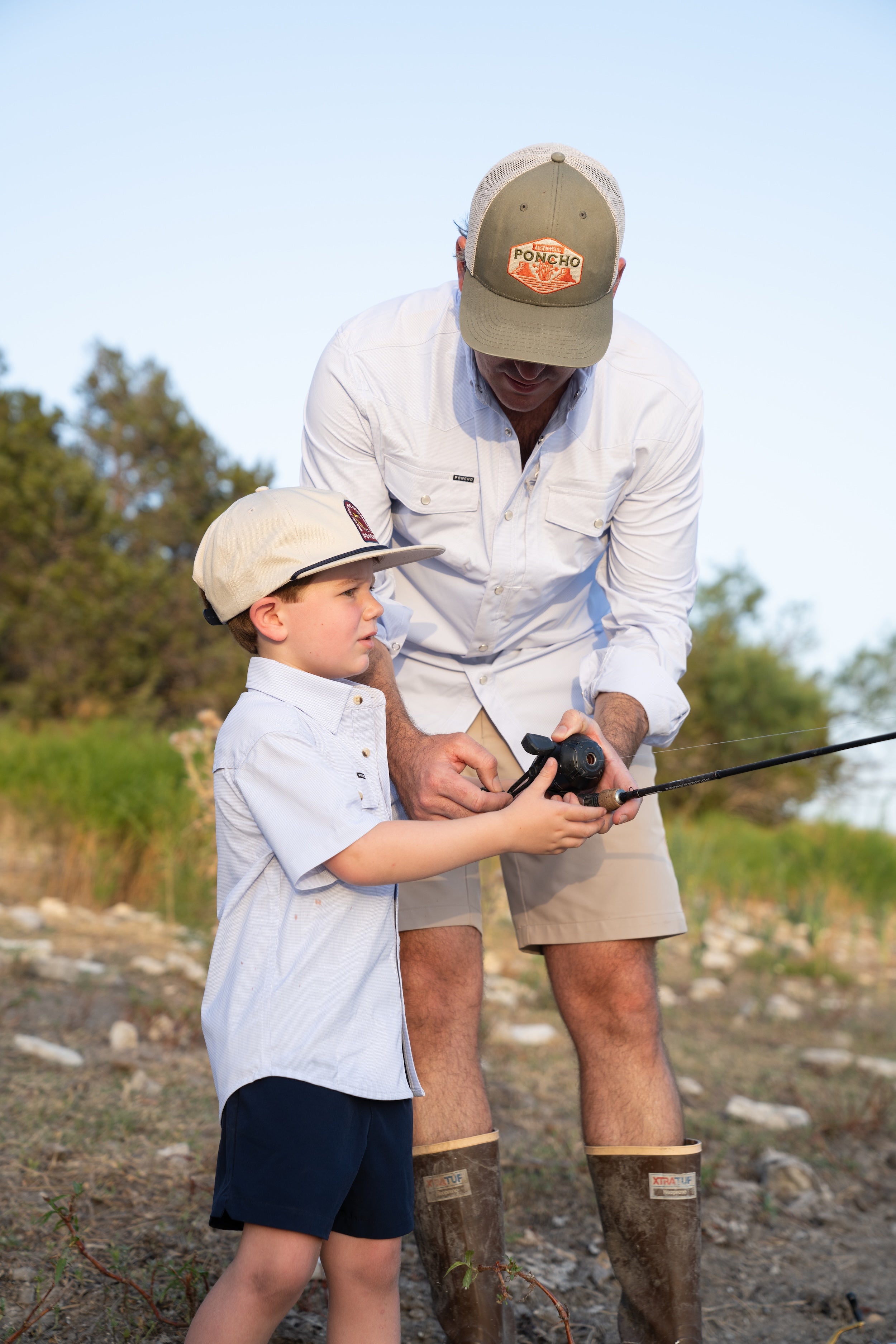 Man and child fishing together outdoors with trees and clear sky in the background