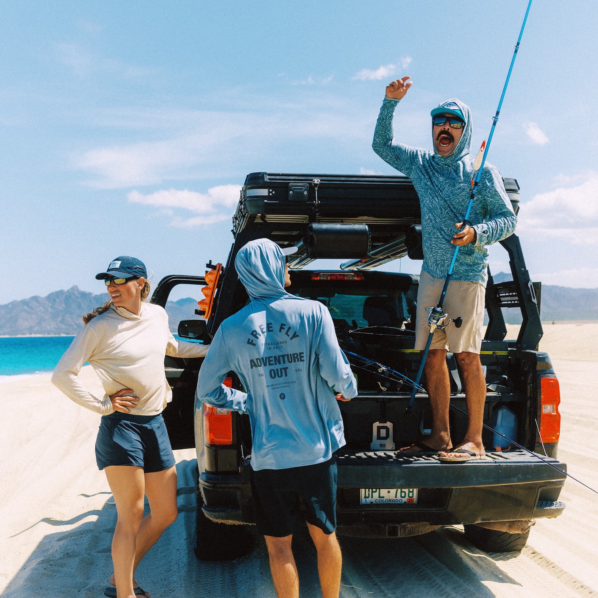People on a beach with a truck, one person holding a fishing rod.