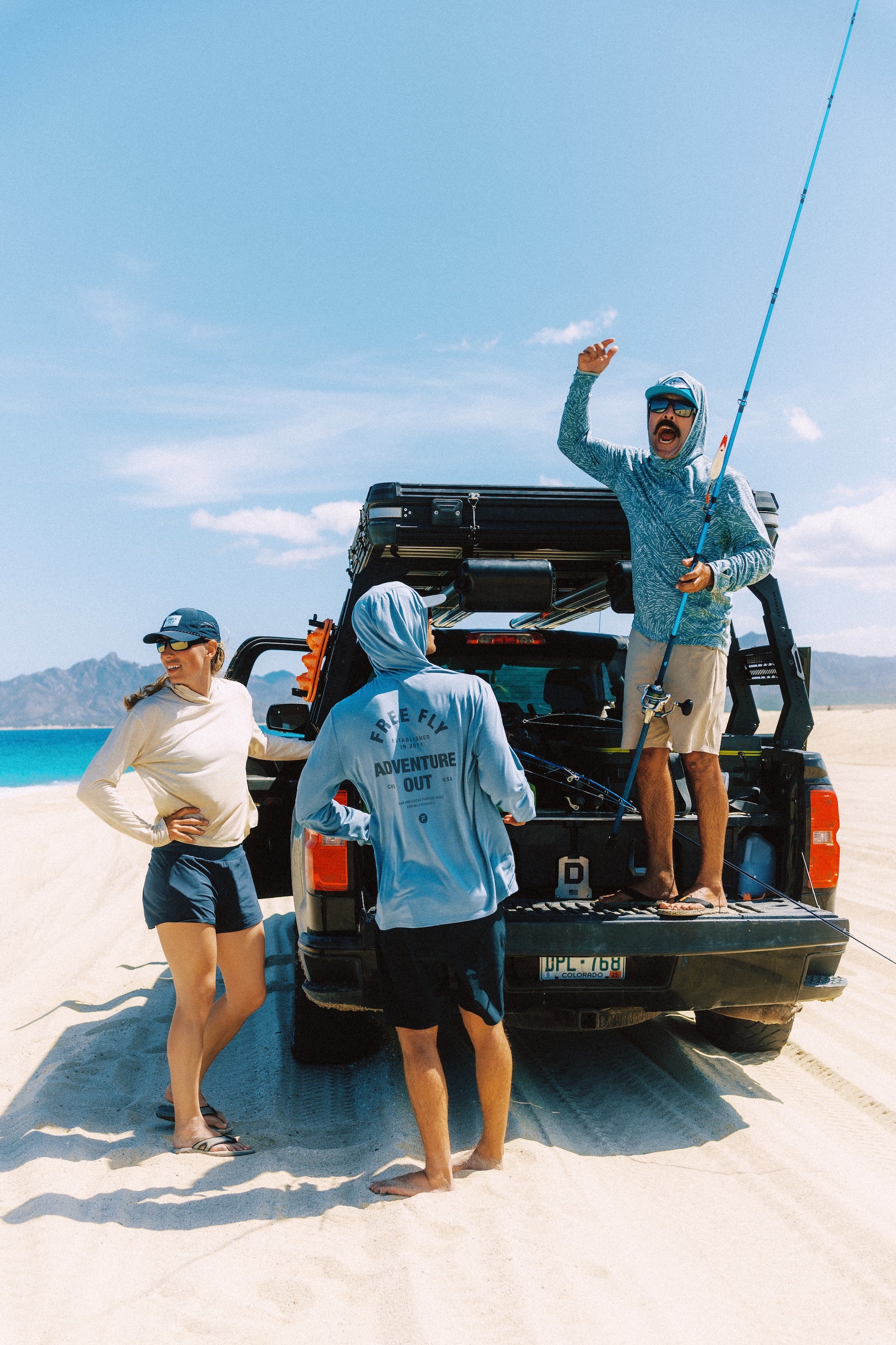 People on a beach with a truck, one person holding a fishing rod.
