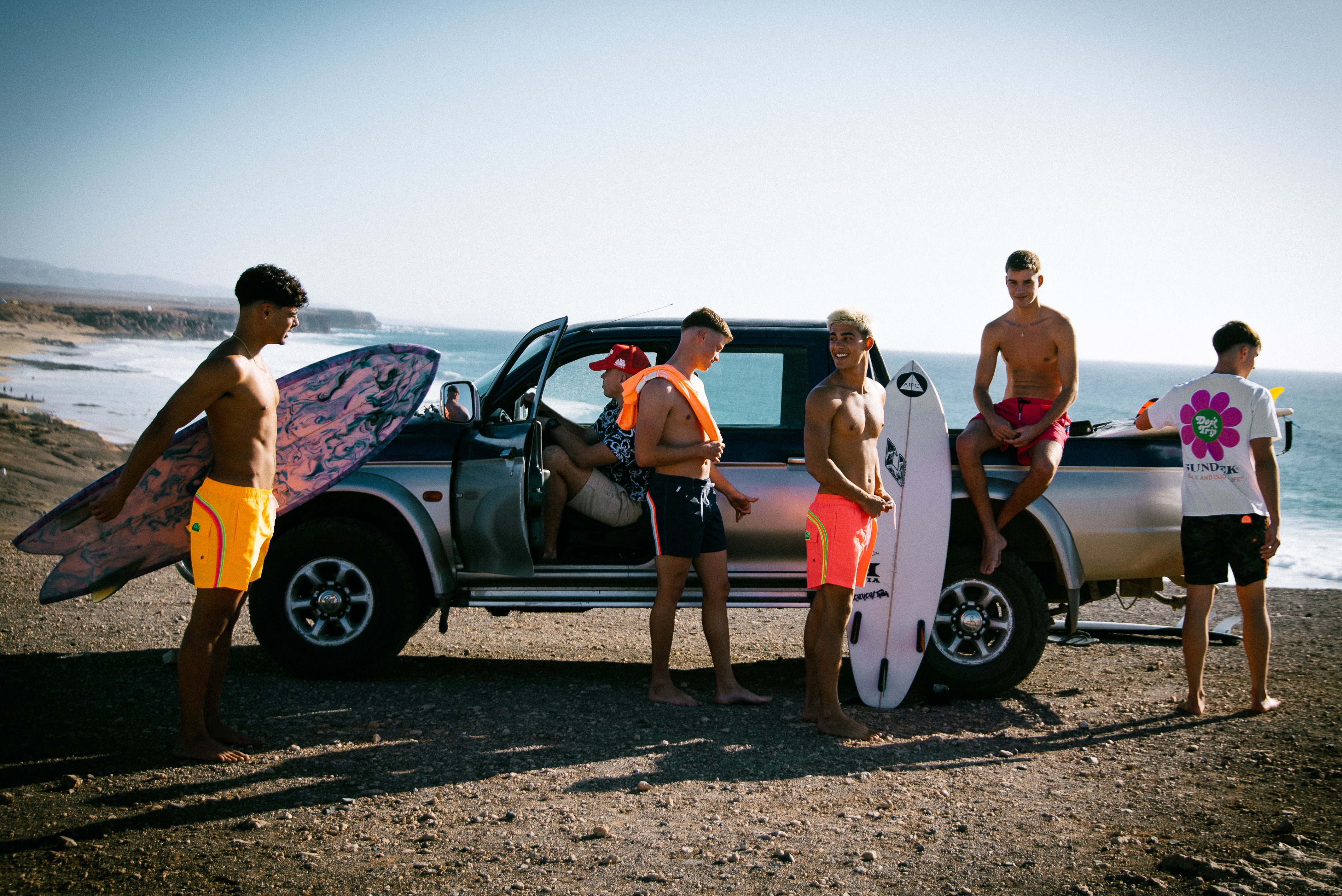 Group of surfers with their boards near a pickup truck by the beach.