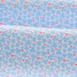 Floral patterned fabric with small blue flowers and pink centers on a light blue background