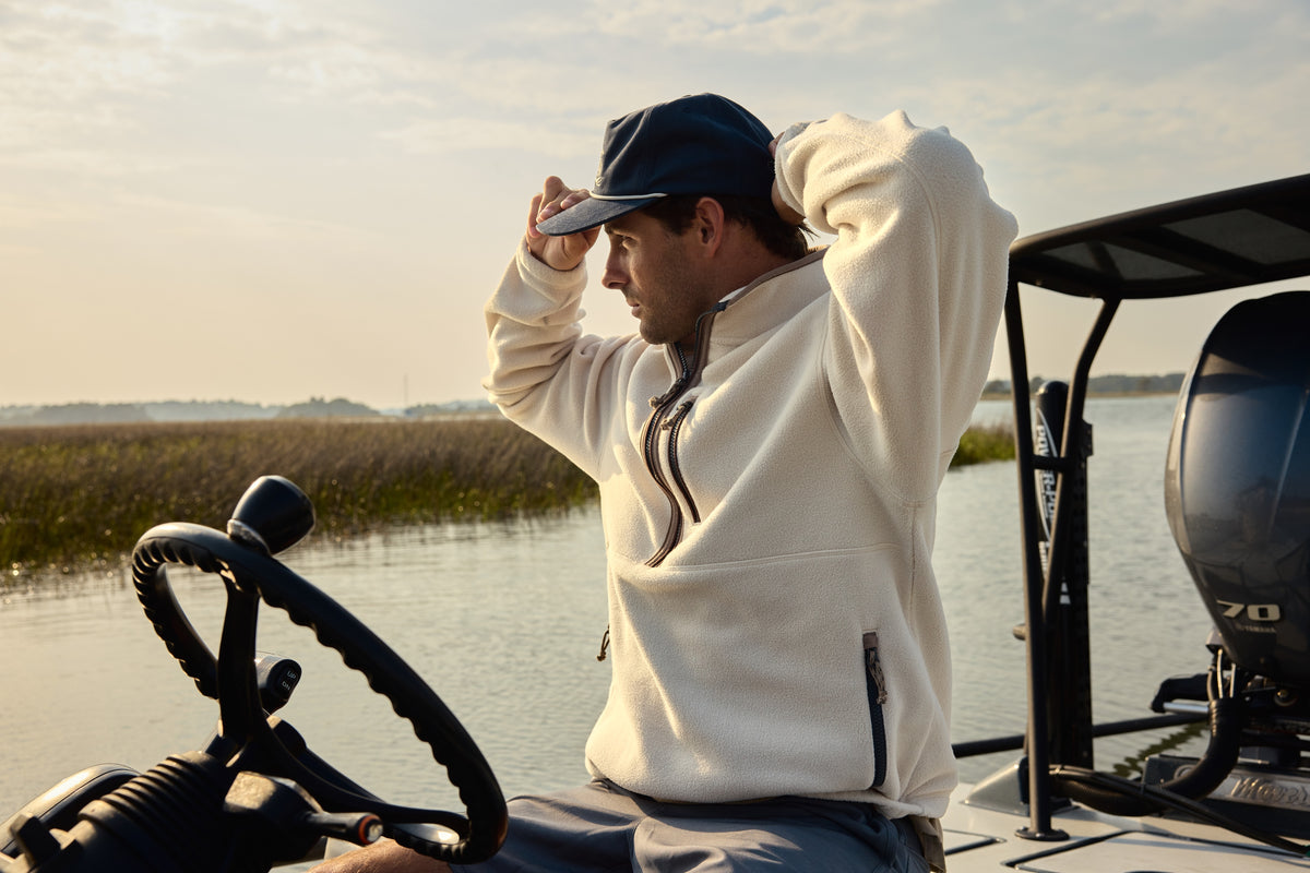 Man on boat in the fleece pullover adjusting hat with the sunset in the background