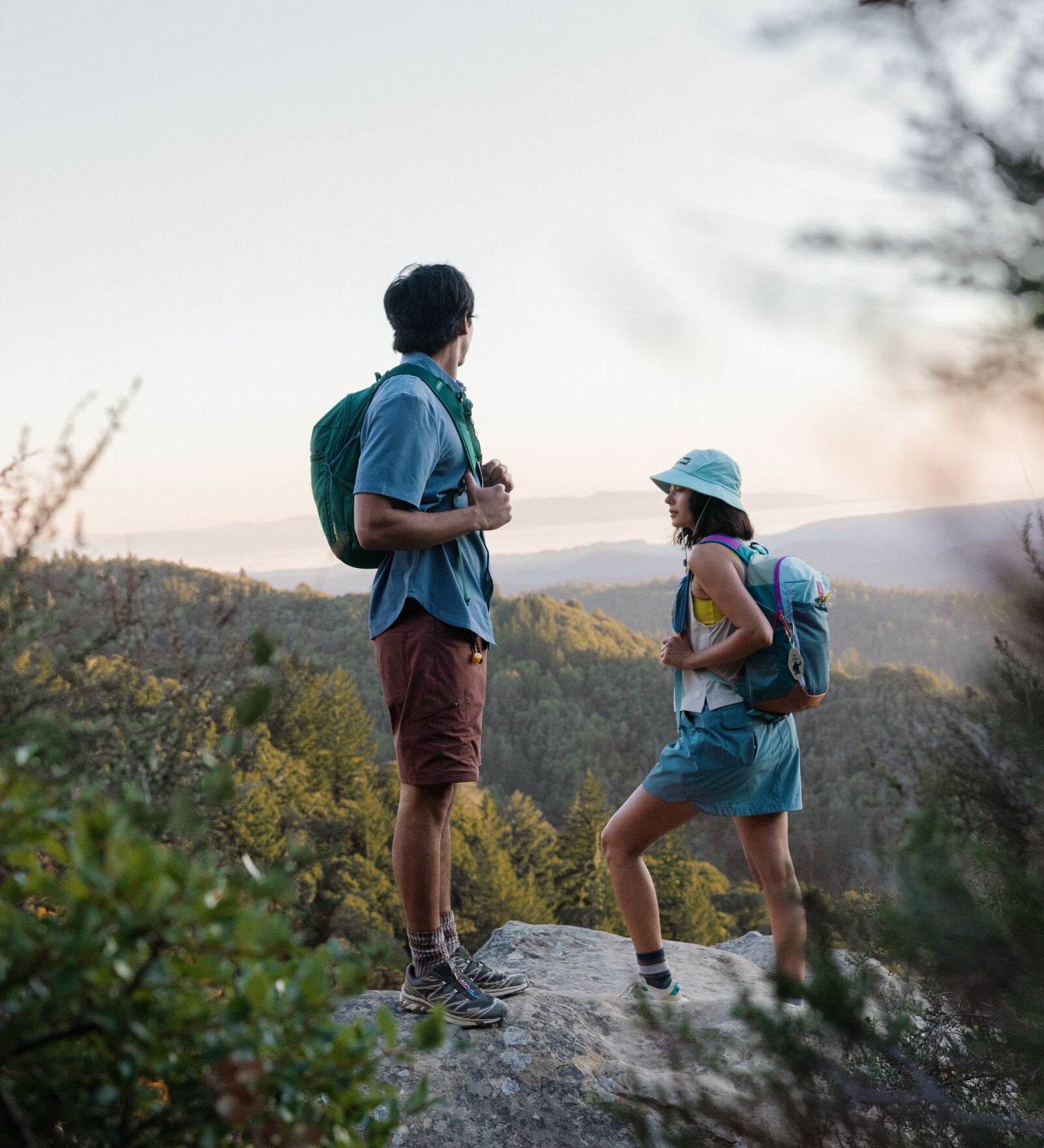 Two hikers with backpacks standing on a rocky outcrop with a scenic background.