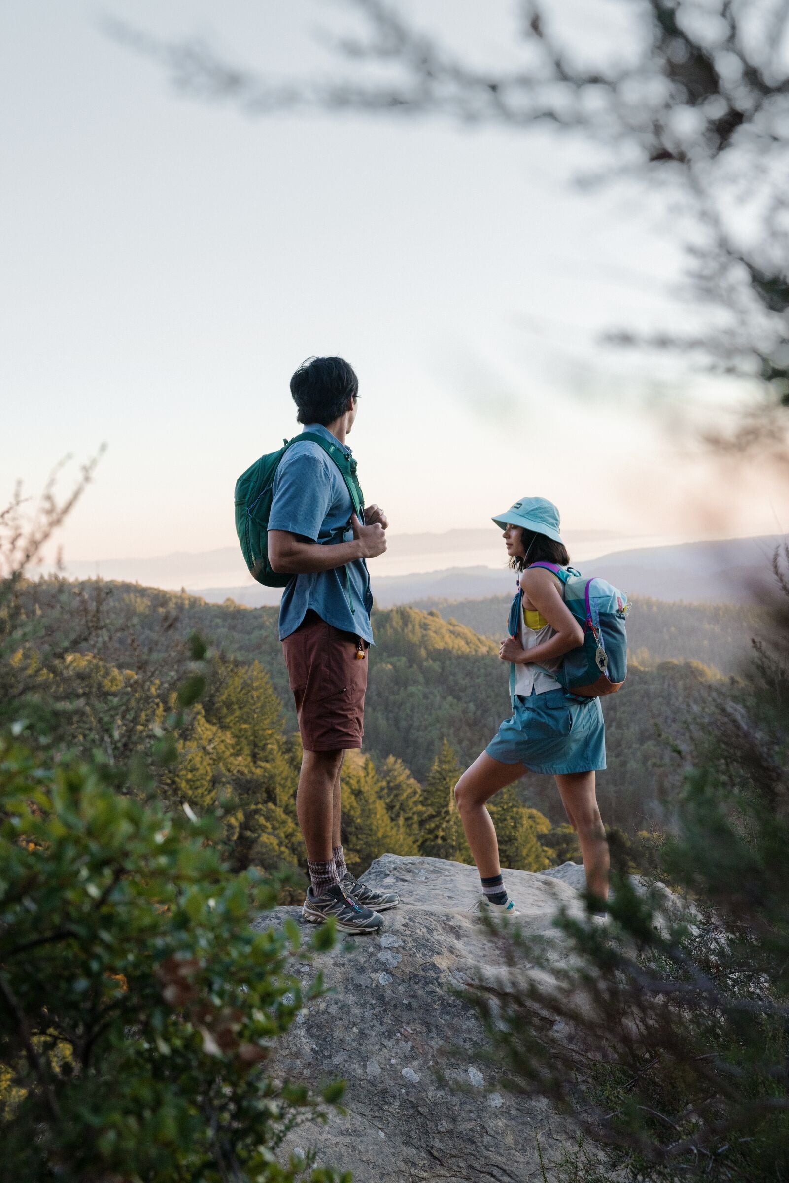 Two hikers with backpacks standing on a rocky outcrop with a scenic background.