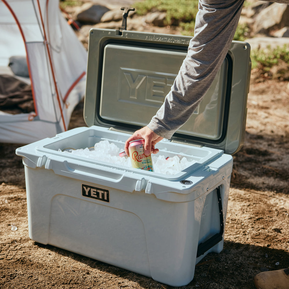 Person opening a YETI cooler with ice and a can, outdoors.