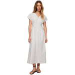 A woman modeling a white midi dress with thin vertical navy stripes, short cap sleeves, and a V-neckline, paired with brown strappy sandals against a neutral beige studio background.