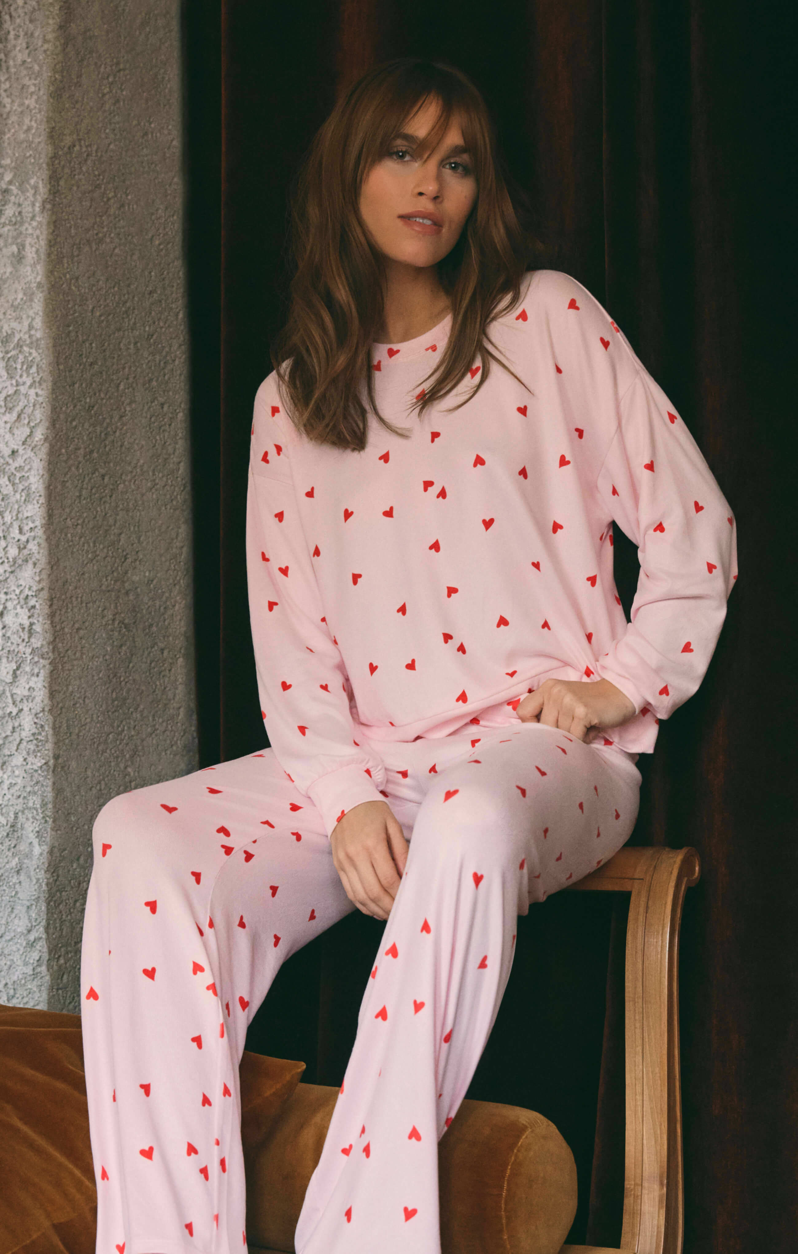 Woman wearing a pink pajama set with red heart patterns sitting on a chair.