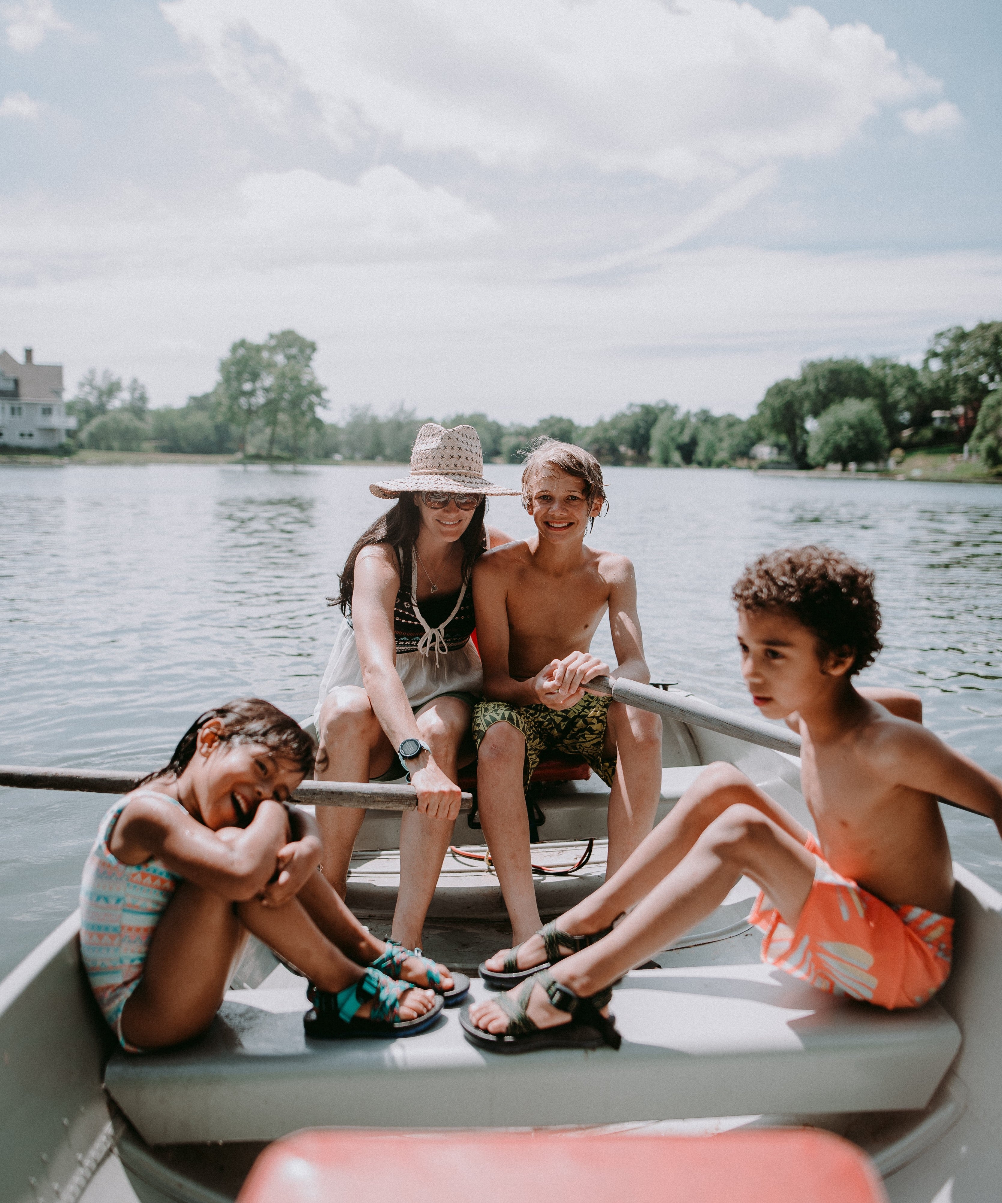 Four children on a boat in a lake with trees and houses in the background