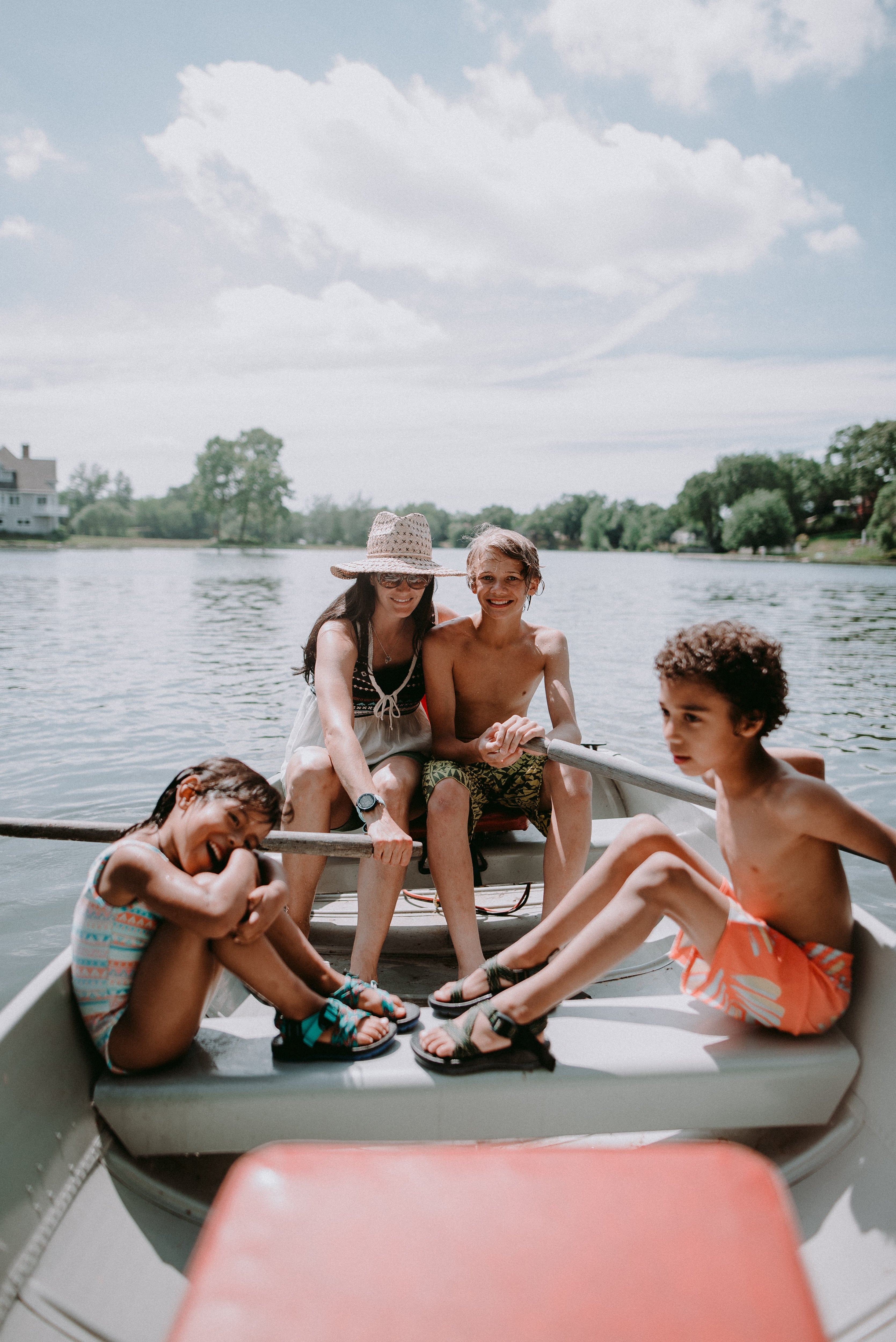 Four children on a boat in a lake with trees and houses in the background