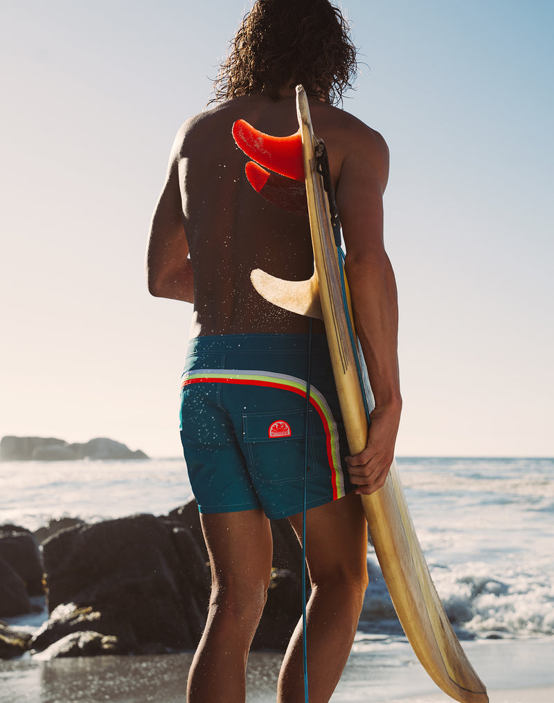 Person holding a surfboard on a beach with ocean and sky in the background