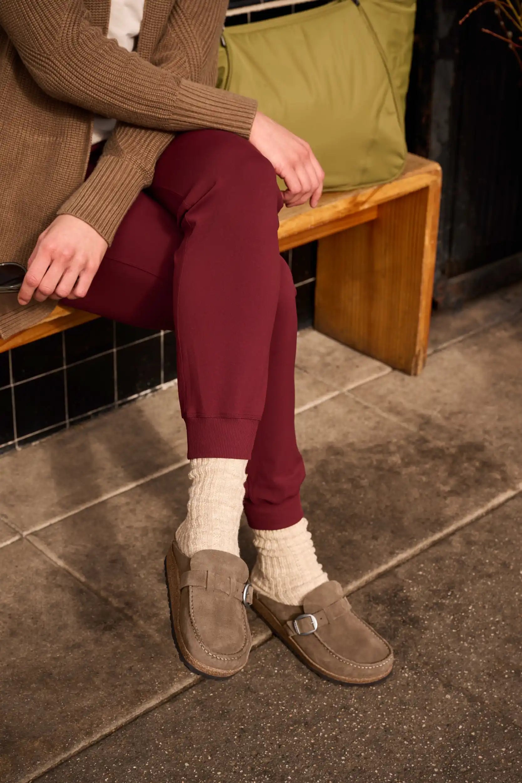 Person wearing burgundy joggers, cream socks, and brown suede loafers.