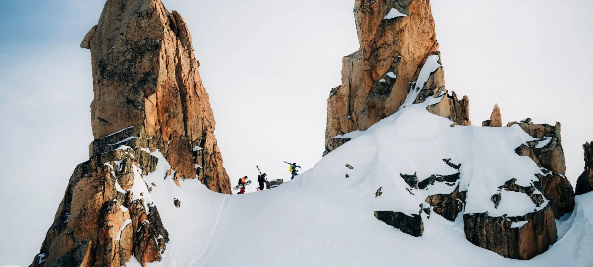 Snow-covered rocky mountain peaks with climbers traversing between them.