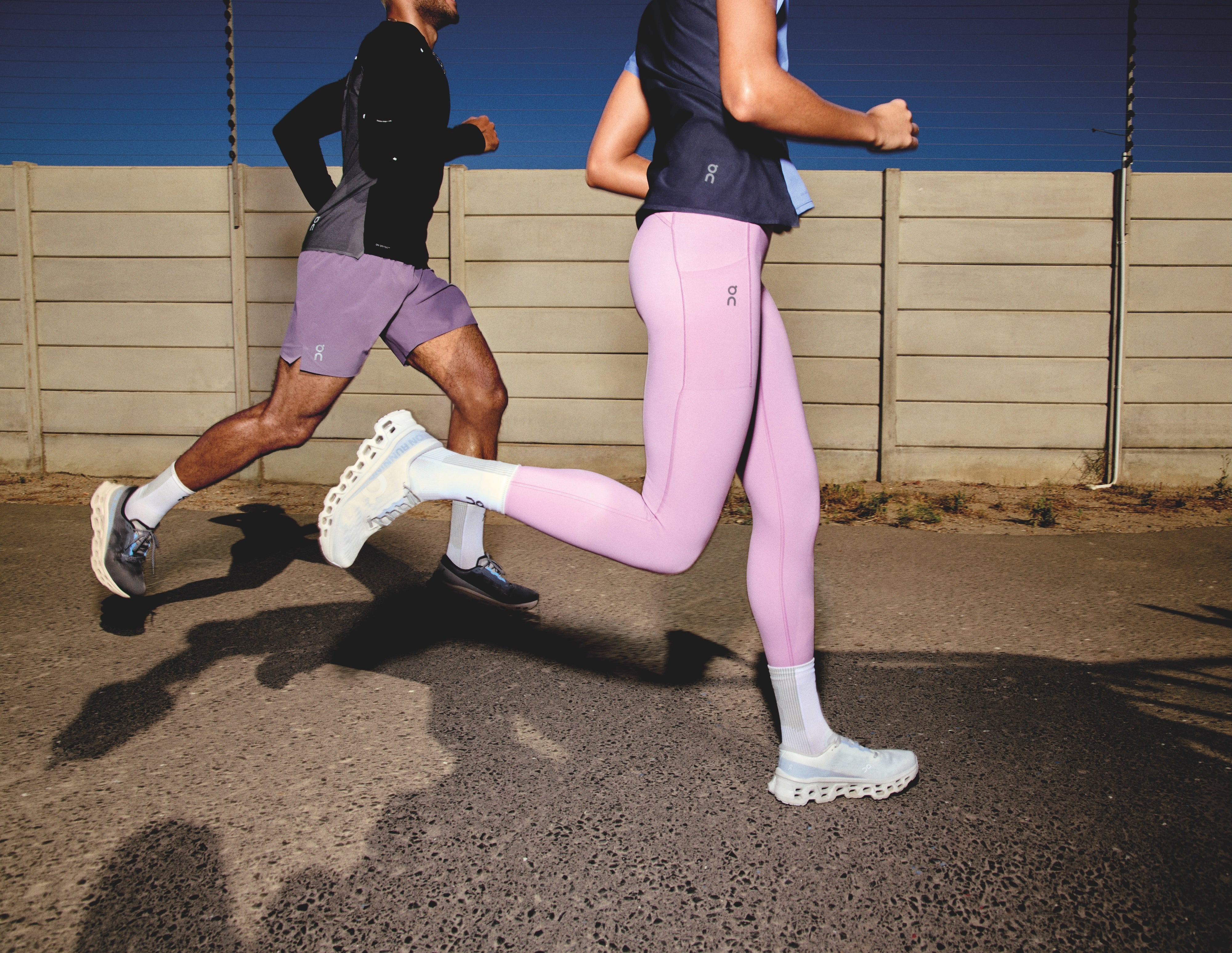 Two runners in athletic wear running on a road with a clear blue sky.
