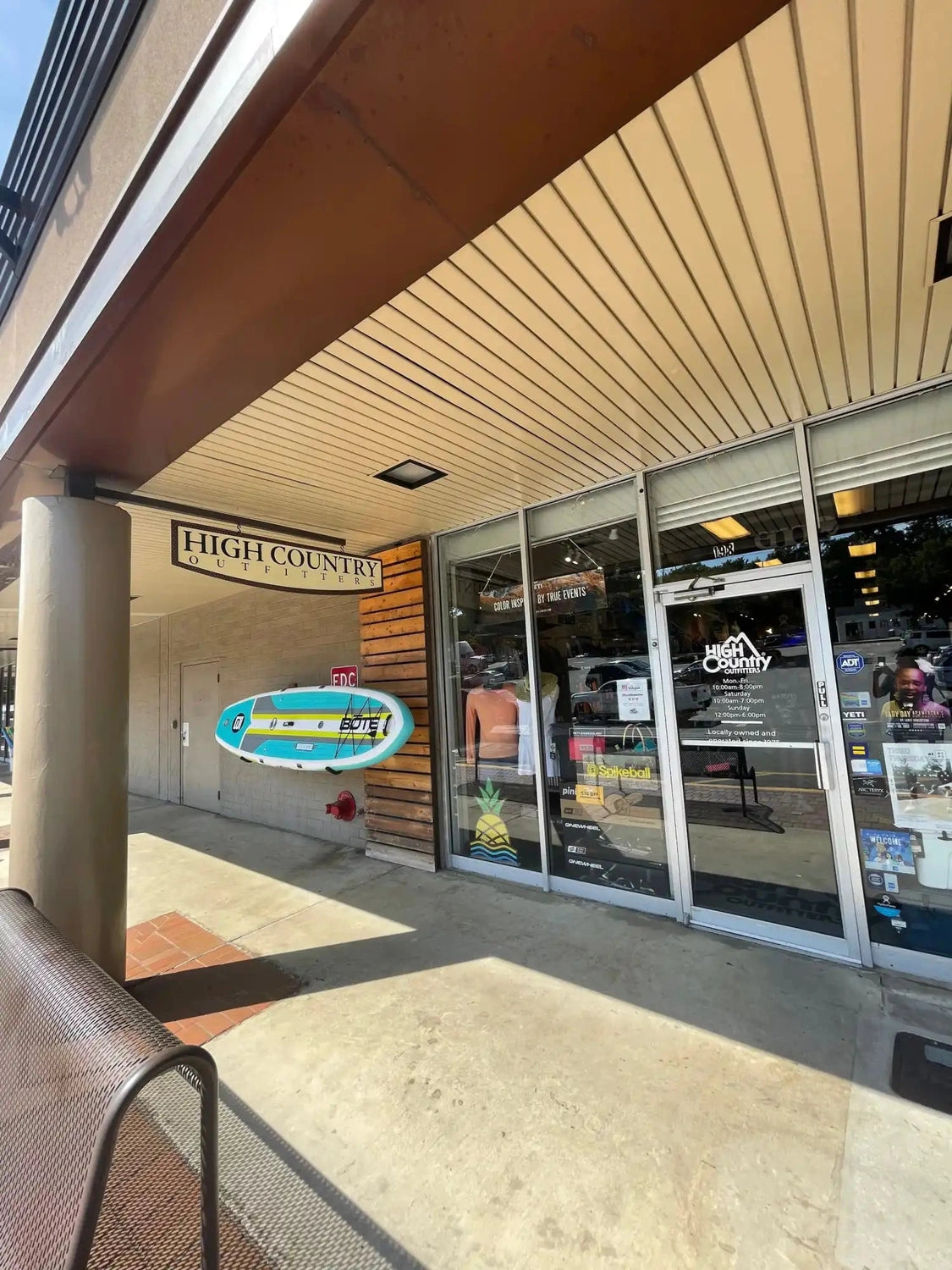 Storefront of High Country Outfitters with a surfboard-shaped sign mounted on the wall.