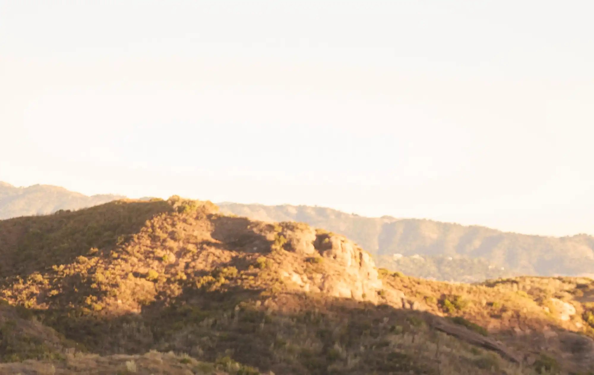 Sun-kissed hills covered in dry vegetation under a bright sky.